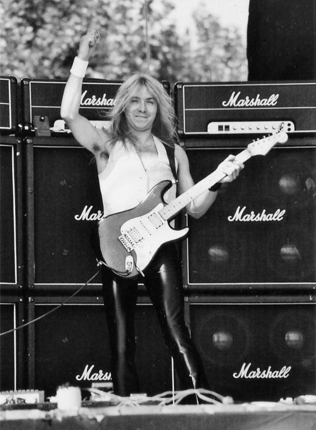 Dave Murray of Iron Maiden performing live in front of stacked Marshall amplifiers.