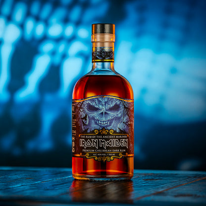 Bottle of Iron Maiden rum with a skull design on a wooden surface and blurred blue background.